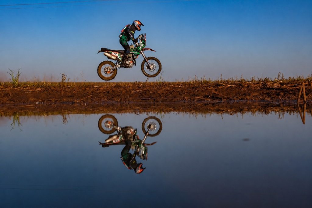 iloto de moto salta em trecho de terra do Sertões Series, refletido na água.